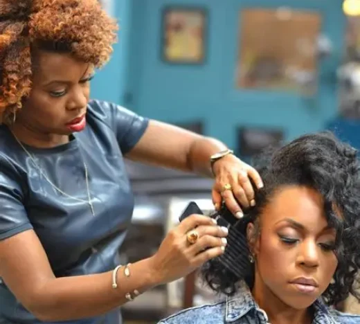 Professional Jamaican hairstylist carefully combs a client’s hair in a salon, symbolizing creative entrepreneurs supported by WILCO Finance’s small business financing.