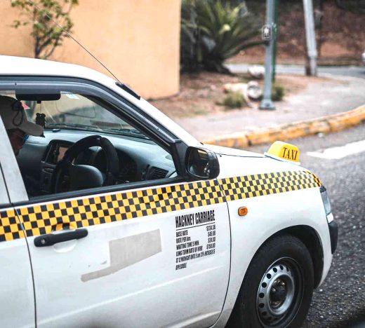 White taxi with yellow checkered stripe and visible fare details parked on a Jamaican street in Kingston, representing transport operators empowered by WILCO Finance MSME loan programs.